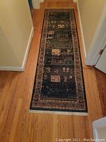 Full view of green Oriental Weavers Sphinx runner rug laid out in hallway over hardwood floors, showing folk art design motifs and border