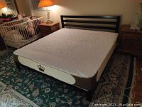 Black wood king size platform bed frame with memory foam mattress and crown emblem cover, set on patterned area rug in bedroom.