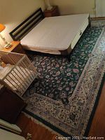 Photo of large green oriental rug placed alongside a bed and wooden furniture showing full design and size relation.