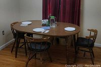 Photo showing oval wooden dining table set for four with plates, water carafe, glasses, and set against burgundy curtains