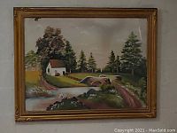 Framed countryside painting showing a rural scene with a house, trees, a road and a stone bridge, in a wood frame with glass.