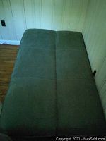 Green fabric convertible sofa bed in sleeper position against a paneled wall on hardwood floor.