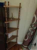 Full view of the wooden corner shelf standing against a wall with five triangular shelves supported by turned wooden pillars.