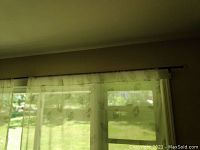 Sheer white curtain panel with leaf pattern installed on black standard size curtain rod, translucent with soft natural light filtering through.