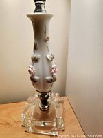 Close-up photo of one lamp's ceramic body with pink and white ceramic flowers and clear glass base