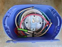 Plastic tub containing coiled garden water hoses in various colors with connectors, some appear new or lightly used