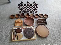 Wood items arranged on carpet showing set of small bowls, divided tray, chopsticks, and small additional pieces with wine rack in the background.