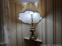 Brass table lamp with scalloped pleated white shade illuminated in corner