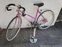 Full view of pink vintage Schwinn track bike with drop handlebars, black saddle, and silver components on asphalt.