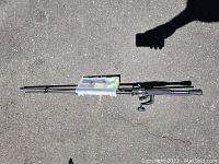 Fishing pole with attached reel and plastic tackle box lying on pavement