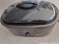 Black Hamilton Beach crockpot with removable lid placed on carpeted floor, showing lid handle and overall condition.