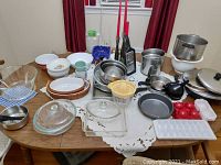 Overview of the lot on a dining table showing vintage Farberware hand mixer, pots, pans, glass bakeware, mixing bowls, and various kitchen accessories.