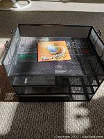 Black metal mesh organizer showing multiple tiers and side hooks with instructional CD inside