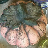 Large pink ceramic pot shaped like a pumpkin with green leaf details on top, showing wear and surface cracks.