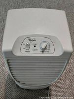 Front view of white Whirlpool Accudry dehumidifier showing vented front panel and control panel with fan speed and dryness control knobs.