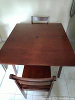 View of the top surface of the solid wood kitchen table with one chair in front, showing the extendable mechanism and surface wear.