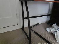 Partial view of black metal table legs, some pieces disassembled, wooden surface edges visible