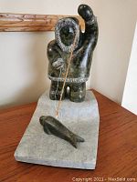 Front view of sculpture showing hunter in parka raising spear over seal on base