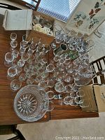 Overview of large vintage glass and crystalware collection on table including various glasses and a large cut crystal bowl.