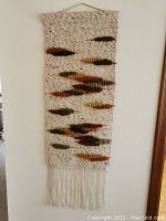 Front view of the full woolen wall hanging on a wall showing its shape, texture, colors, and hanging method.