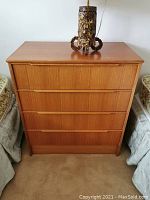 Full frontal view of the five-drawer teak veneer lowboy dresser with lamp on top.