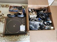 Overall view of the lot showing the Dual turntable with dust cover, two Sennheiser headphones, and the box with various cables and accessories on a patterned surface.