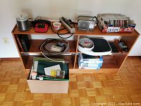 Overall lot showing shelving unit with various miscellaneous items including CDs, scale, radio, phone, office supplies, and a box containing papers and binders.
