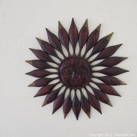 Full view of the painted metal sun-figure wall hanging mounted on a wall, shows overall shape and size.