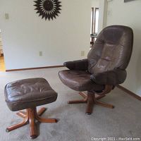 Brown leather lounge chair with padded armrests on star-shaped wooden swivel base, paired with matching footrest