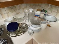 Assorted vintage/used dishes, glassware, and kitchenware displayed on kitchen counter including bowls, pitchers, jars, and trays.