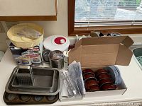 Overview of assorted vintage kitchenware items on counter including containers, baking pans, and a boxed ice cream maker.