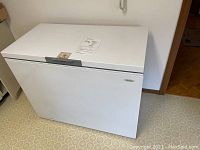 White Whirlpool chest freezer closed and standing on a kitchen floor with vinyl tile pattern.