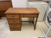 Full view of Vilas maple single pedestal desk showing three drawers on left and writing surface on right with light red marks visible on top surface.