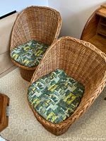 Two wicker tub chairs side by side on hexagon-patterned flooring with green printed cushions.