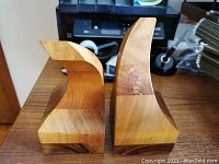 Photo showing both wooden bookends from side angle on wood surface, highlighting the curved top design and wood grain.