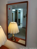 Full view of rectangular wall mirror with teak frame leaning against wall