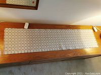 Full view of vintage woven table runner laid on wooden surface showing overall length and design with a white remote for size reference.