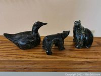 Three carved soapstone animal sculptures displayed on wooden surface including bird, walking bear, and sitting bear.