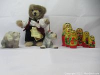 Full lot photo showing teddy bear, Matryoshka dolls, and stone bear figurine arranged side by side on white background.