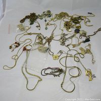 Overview of assorted costume jewelry laid out on white surface showing chains, pendants, and bracelets in varying styles and conditions.