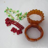 Four pieces of vintage costume jewelry on white background: two brown stretch bracelets, one red linked bracelet, and one white and green beaded necklace.