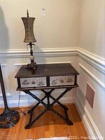 Front view of wooden table with two crackle finish drawers and ornate table lamp on top.