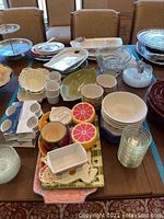 Full lot of assorted kitchenware items on a dining table including bowls, plates, ramekins, glass bowls, fruit-shaped containers, and serving platters.