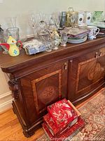 Sideboard surface displaying multiple glass and crystal barware items, pewter stein, mugs, and a battery powered anniversary clock.