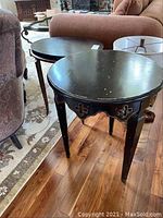 Two black wood end tables, round and oval, with distressed finish and surface scratches