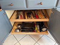 Two kitchen cabinet drawers containing multiple grilling and cooking utensils laid out separately to show contents.
