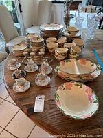 Full overview of Franciscan Desert Rose dishware and serving pieces arranged on wooden table, including tea cups, saucers, and aperitif glasses.