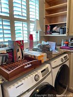 Wide view of stacked party supplies, boxed fondue, wooden tray on countertop above Samsung washer and dryer