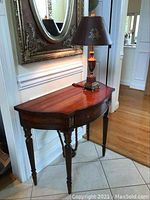 Full view of half-moon table with turned legs and decorative table lamp placed on top