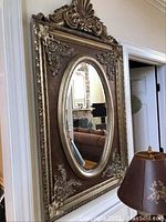 Full view of ornate wall mirror leaning against wall with adjacent furniture.